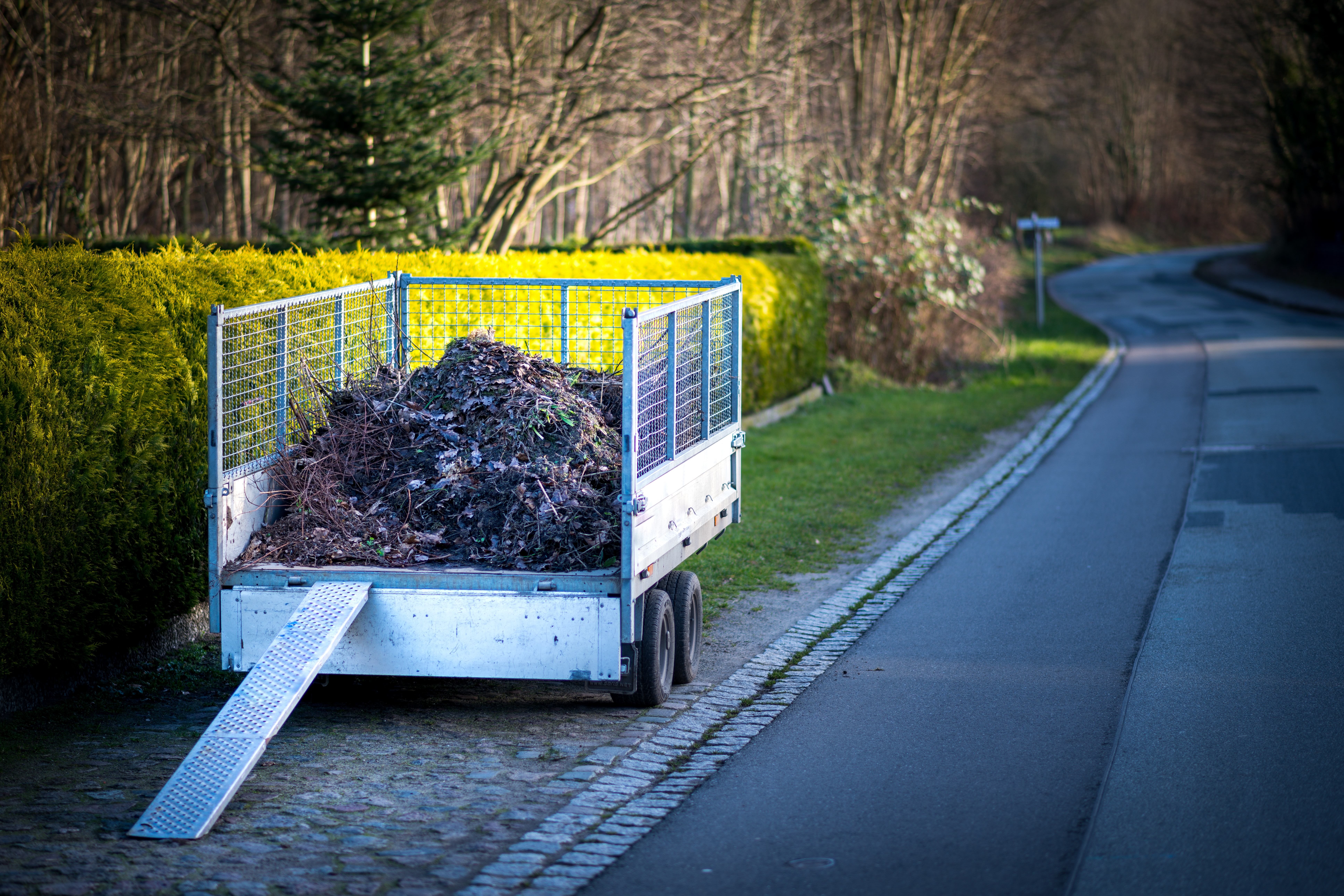 Kompost und Gartenabfälle auf einem Anhänger mit Rampe für eine Schubkarre.