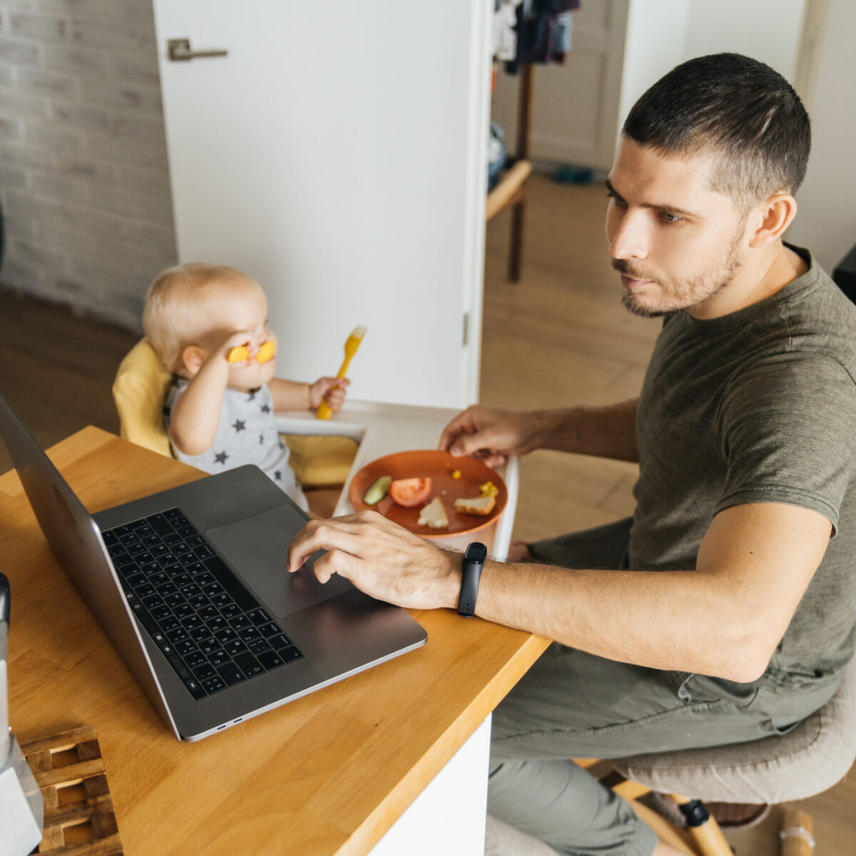 Feeding a baby in a modern family. Male Dad and his daughter in the kitchen interior. Remote work and difficulties of education.