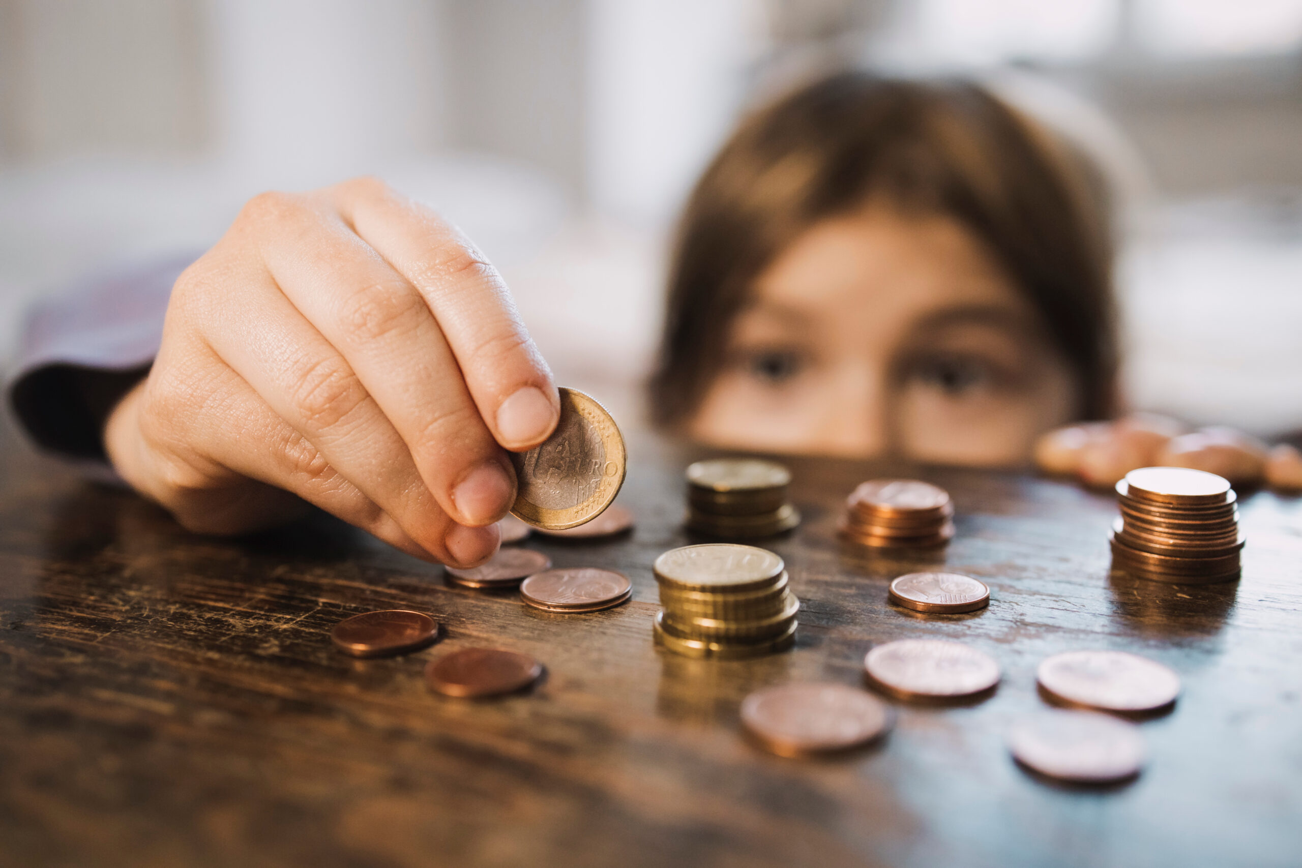 Ein Kind schaut über eine Tischkante. Auf dem Tisch liegen einige Euro-Münzen, die das Kind vorsichtig in die Hand nimmt.