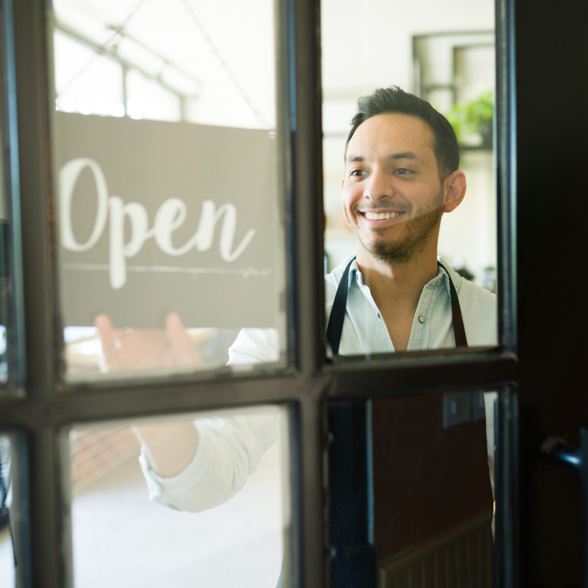 Fröhlicher Geschäftsbesitzer dreht Öffnungsschild von "Geschlossen" auf "Geöffnet"